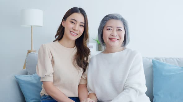 Portrait of Asian lovely family, young daughter sit on sofa with older mother in living room at home