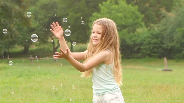 Cheerful Girl Plays Catch Soap Bubbles on the Meadow. Slow Motion. Close Up