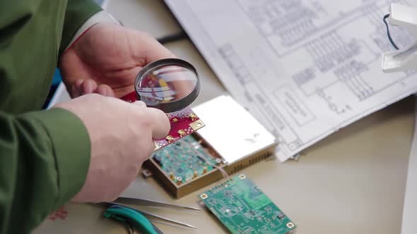 A Man Using a Magnifying Glass Checks Quality of Soldering on an Electronic Board. Quality Control