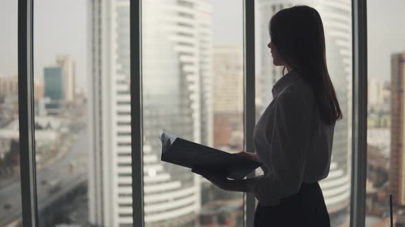 Silhouette of an Attractive Girl with a Folder for Papers in Her Hands