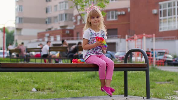 Stylish Little Child Kid Play with Trendy Pop It Bubble Squishy Sensory Toy Game on Playground Bench