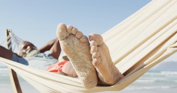 Happy senior african american man lying in hammock on sunny beach
