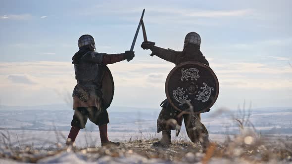 Two warriors viking are fighting with axes and shields on the winter meadow.