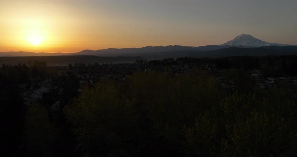 Aerial shot rising up through trees to reveal the sunrise and Mount Rainier on the horizon.