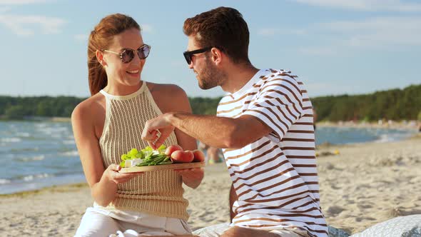 Happy Couple with Food Having Picnic on Beach