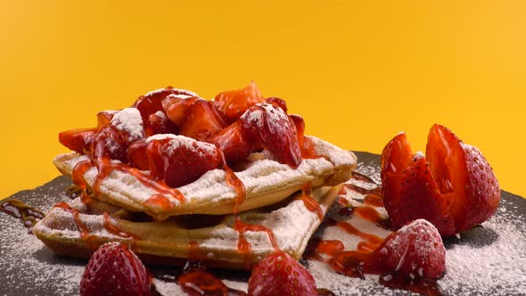 Belgian waffles with strawberry, sweet strawberry topping and powdered sugar on a stone board