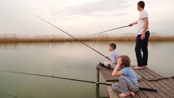 Dad and Son and Daughter on a Wooden Bridge Catch Fish From the River