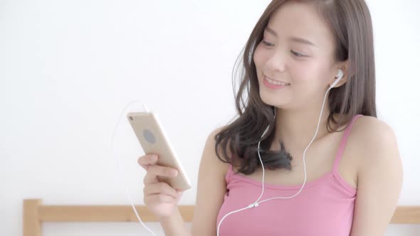 Beautiful young asian woman enjoy listen music with earphone and holding smart phone.