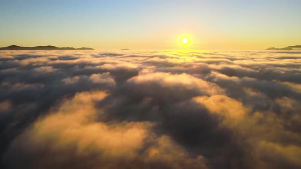 Aerial View of Colorful Sunrise Over White Dense Fog with Distant Dark Silhouettes of Mountain Hills