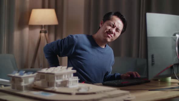 Asian Male Engineer With The House Model Having A Backache While Working On A Desktop At Home