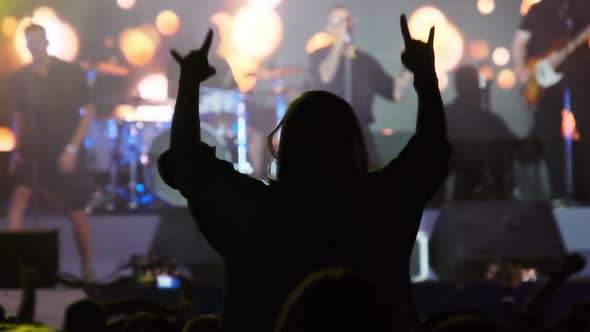 Silhouette of Woman in Crowd at Rock Concert Showing Sign Devil's Horns Gesture