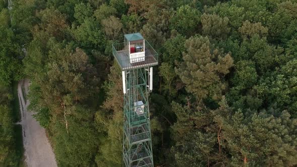 Tall steel forest observation tower and dirt road, fly out aerial drone view