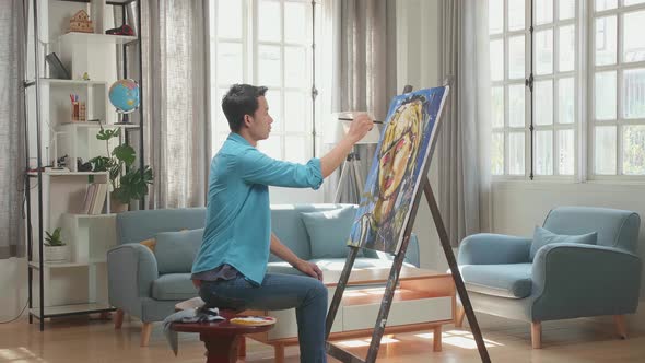 Asian Artist Man Sitting And Painting A Girl's Hair On The Canvas