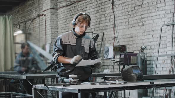 Young Man in Protective Glasses Working at the Plant  Riding the Instruction on the Piece of Paper