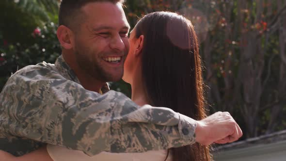Smiling caucasian male soldier embracing his happy wife in garden outside their house