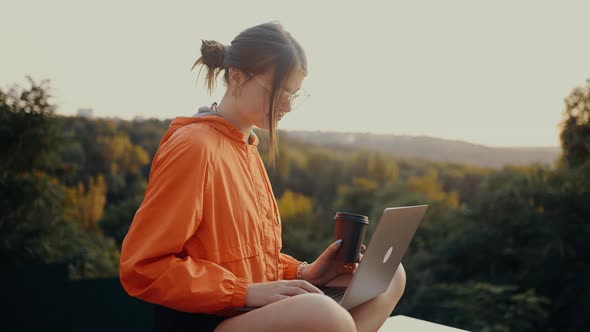 The Concentrated Girl Does the Shopping Online in the Park Through the Computer with a Cup of Coffee