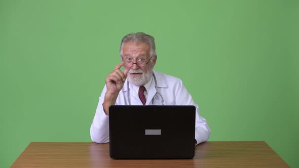 Handsome Senior Bearded Man Doctor Against Green Background