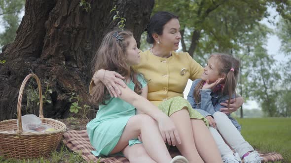 Portrait Elegant Senior Woman Sitting on the Grass Under the Tree in the Park Hugging Granddaughters