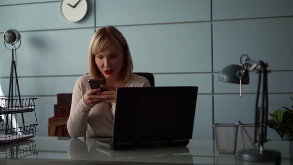 A Close-up Portrait of a Middle-aged Woman with Blond Hair, Sitting in an Office at a Laptop on a