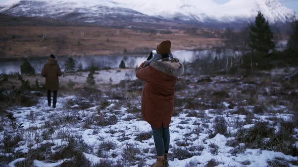 Two Tourists Walking in Slow Motion Through the Countryside Towards the Snowy Mountain Peaks on the