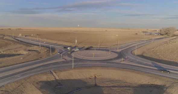 A roundabout in the middle of the countryside, cars and trucks slow to navigate the circle.