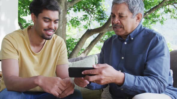Man sharing smart phone with young son while sitting together at patio