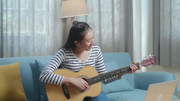 Asian Woman Learning Playing Guitar By A Laptop At Home