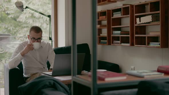 Young Businessman Drinking a Cup of Coffee and Working on a Laptop