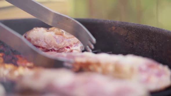 Slow Motion of Tongs Flipping Sizzling Meat on Fiery and Smokey BBQ Grill