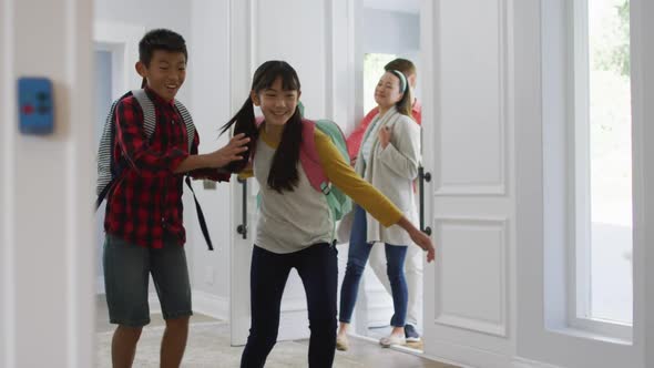 Excited asian son and daughter running through front door, returning home with parents