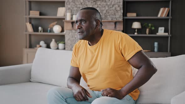 Senior African American Man Sit on Cozy Sofa Relaxing in Living Room Hold Remote Control Switch