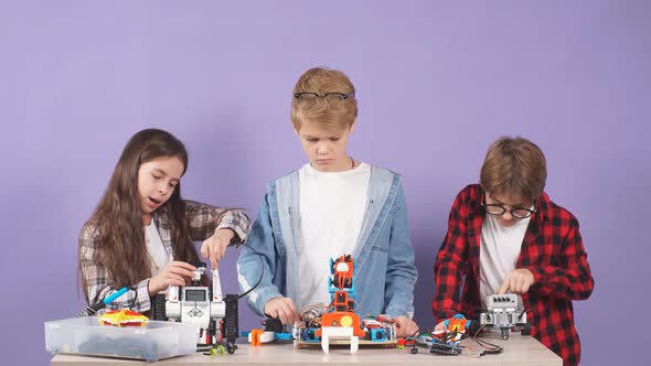 Caucasian Kids Try To Connect Wires and Assemble Robot Isolated Over Purple Background