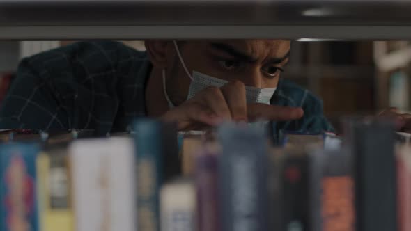 Closeup Serious Focused Young Indian Guy in Medical Mask Looking for Suitable Book in Bookstore