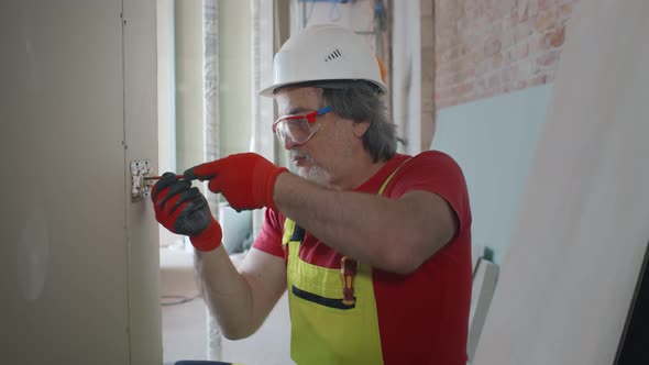 Mature Electrician at Work with Wall Outlet and Screwdriver Installing Sockets