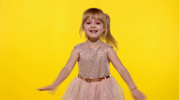 Little smiling blonde child kid girl waving greeting hello hi with hand on yellow background
