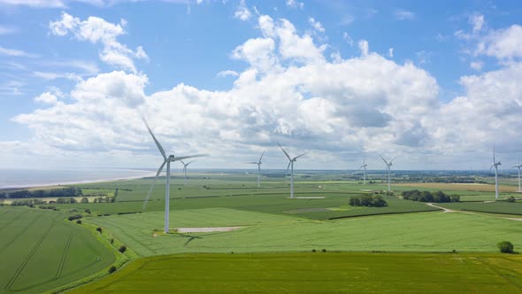 Aerial hyperlapse of Wind Turbines and Clouds with the wind making waves in the fields.