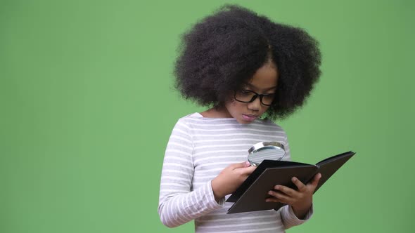 Young Cute African Girl with Afro Hair Studying Against Green Background