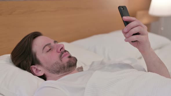 Casual Young Man Using Smartphone While Sleeping in Bed