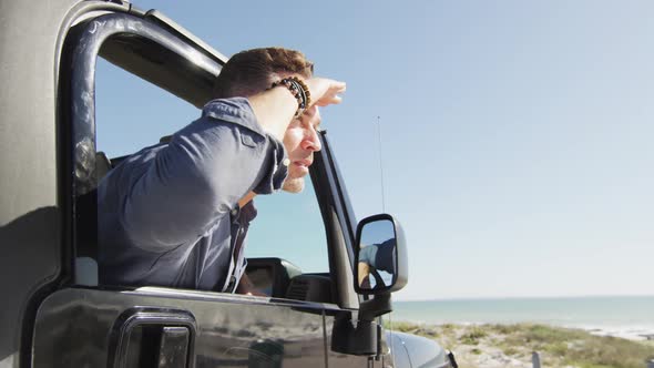 Happy caucasian man in car admiring the view on sunny day at the beach