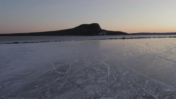 Ice protected by breakwater on a lake at dawn with mountain in distance AERIAL