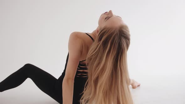 A Spectacular Young Girl Sits with Her Back in a White Studio and Turns Her Head to the Camera While