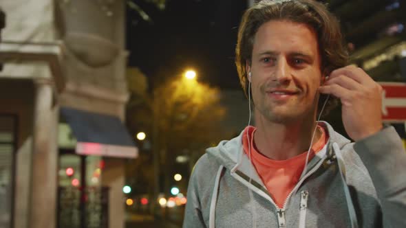 Caucasian male doing sport, smiling, putting on earphones in a street in the evening