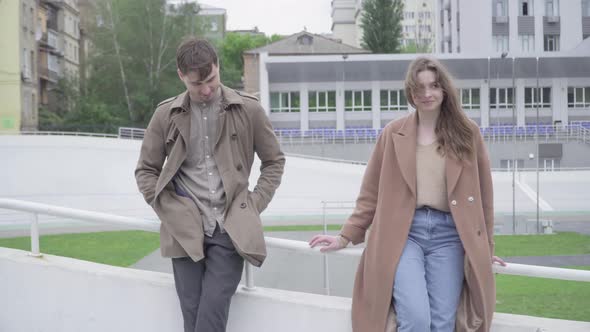 Portrait of Shy Caucasian Man and Woman Touching Hands As Standing Outdoors on City Street. Young