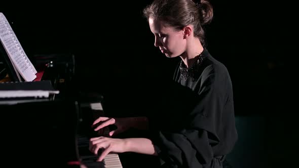 A young woman plays the piano energetically in the spotlight on the stage