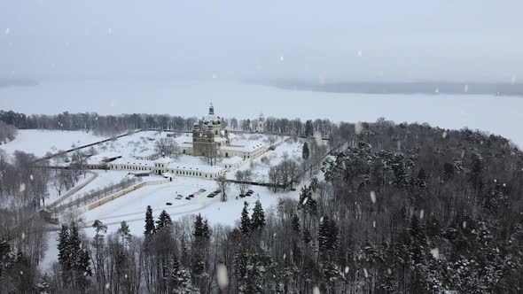 Frozen white Kaunas lagoon and Pazaislis monastery covered in snow during heavy snowfall, aerial dro