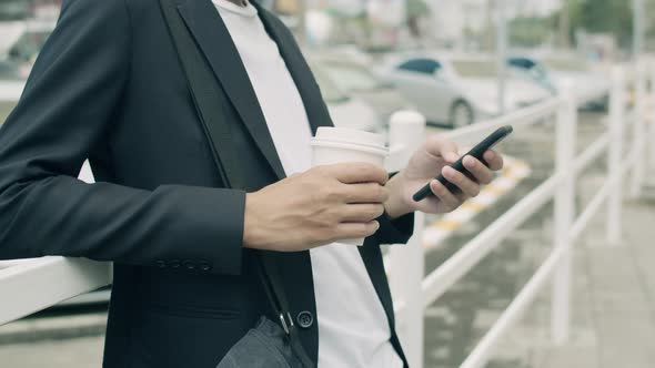 Young businessman using smartphone while standing beside the fence on the street in a city.