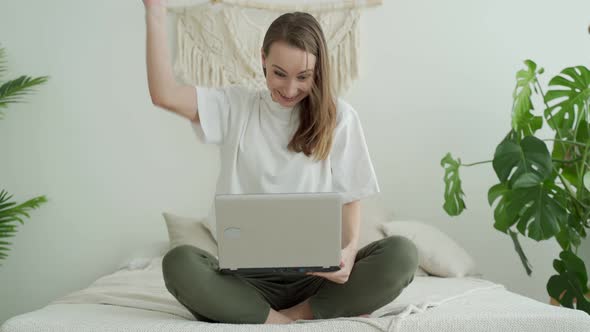 Young Woman Sitting on the Bed with Laptop Celebrating a Victory or Success