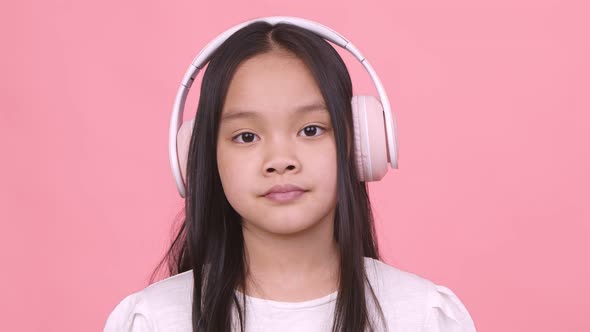 Close Up Portrait of Little Asian Girl Wearing Big Wireless Headphones Pink Studio Background