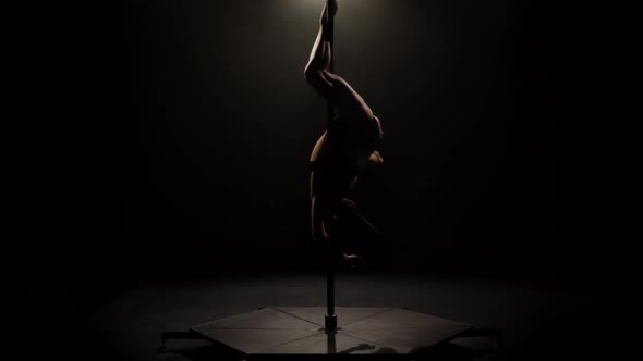 Dancer Spinning on a Pole . Black Background. Slow Motion. Silhouette