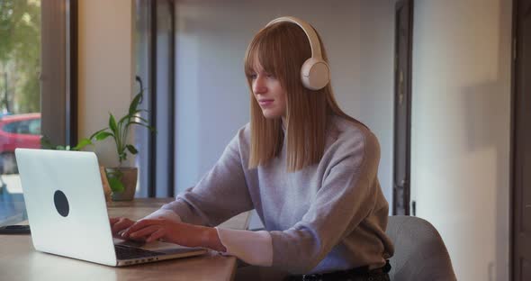 Blonde Woman in White Headphones Typing Message on Laptop Sitting in Cafe